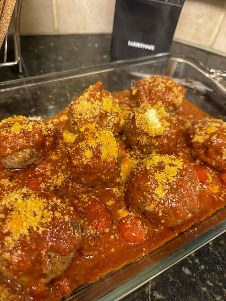 Tray of homemade meatballs in tomato sauce, dusted with parmesan